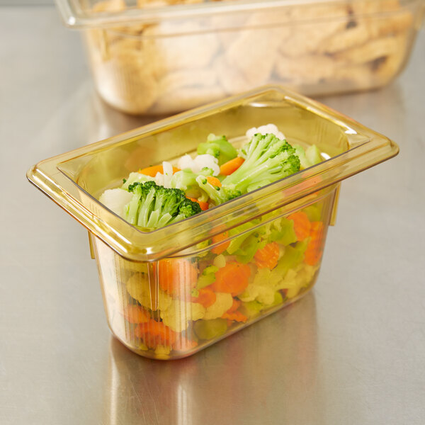 A close up of a Vollrath 1/9 size amber high heat plastic food pan with broccoli and carrots inside.