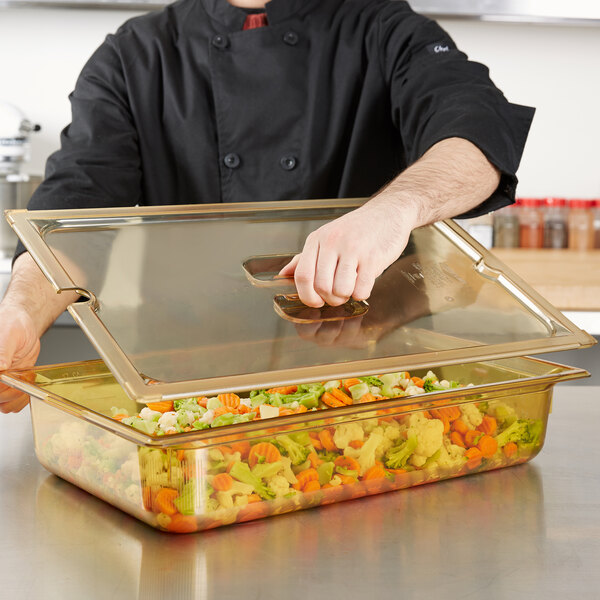 A person holding a Vollrath Super Pan lid over a glass container of vegetables.