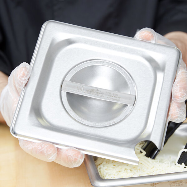 A person holding a Vollrath stainless steel slotted cover on a metal container full of cheese.