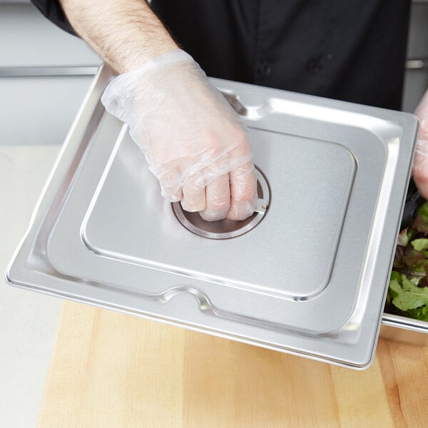 A person in plastic gloves placing a Vollrath stainless steel cover on a tray of food.