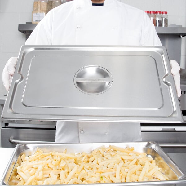 A chef in a white coat holding a silver tray of french fries.