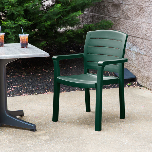 A green Grosfillex Acadia resin armchair on a concrete patio next to a table with drinks on it.