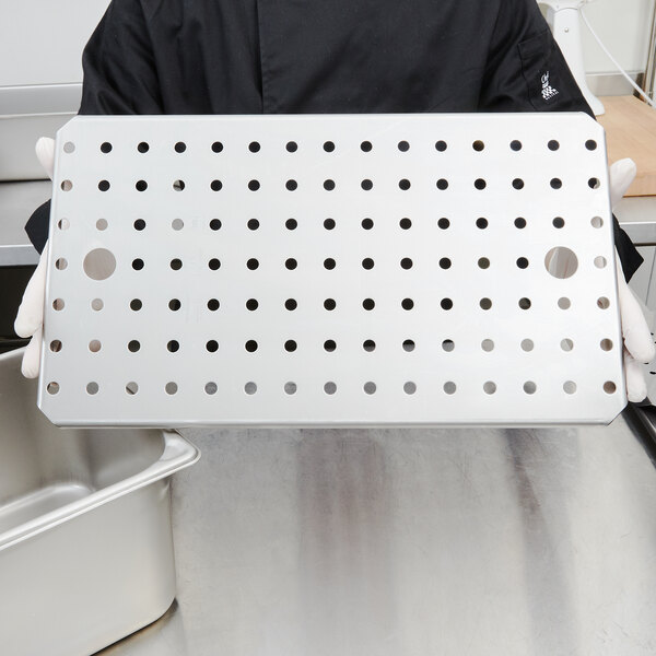 A person holding a Vollrath stainless steel tray with holes in it.