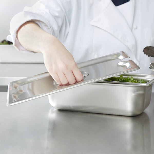 A hand using a Vollrath stainless steel slotted cover on a metal container.
