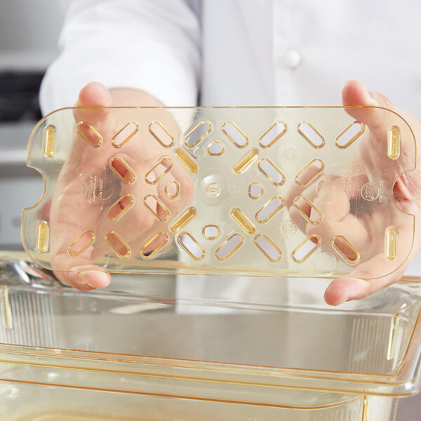 A person holding a Vollrath high heat plastic drain tray on a counter.
