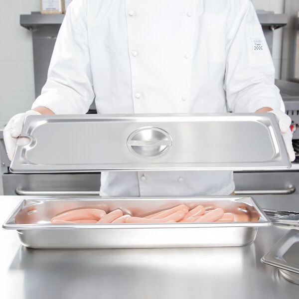 A chef holding a Vollrath stainless steel slotted cover over a stainless steel tray of sausages.