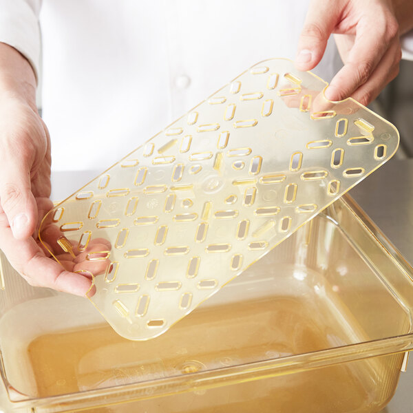 A person holding a Vollrath amber plastic tray with holes in it.