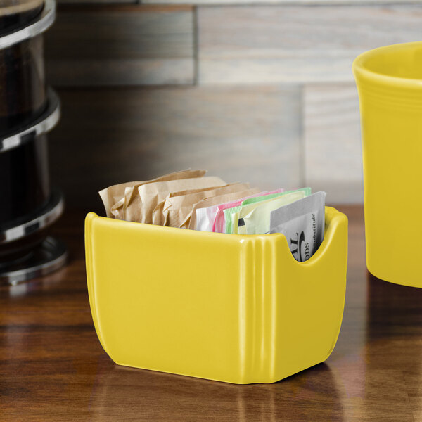A yellow Fiesta sugar caddy on a counter with packets inside.