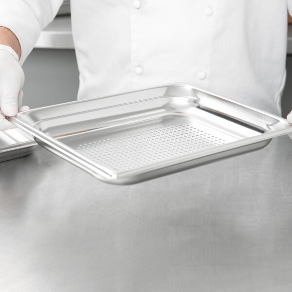 A chef holding a Vollrath stainless steel steam table pan on a metal tray.