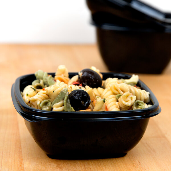 A close-up of a Sabert black square deli bowl filled with pasta and olives.