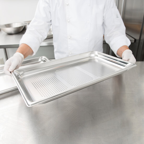 A chef holding a Vollrath stainless steel tray with a perforated pan on it.