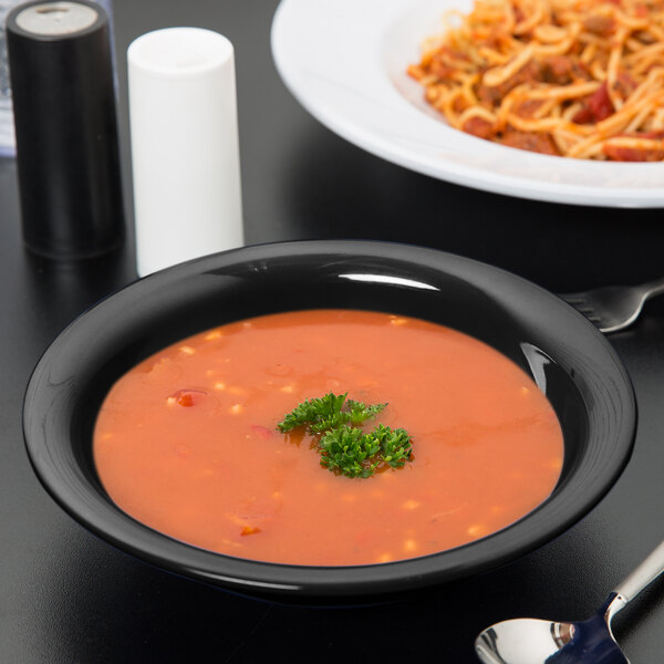 A Carlisle black rimmed melamine bowl of soup with a spoon on a table.