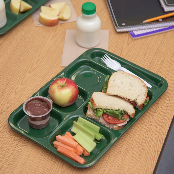 A Carlisle forest green 6 compartment tray on a table with a sandwich, apple, carrot, and other food.