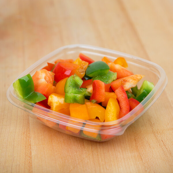 A Sabert clear plastic square bowl filled with chopped green and red bell peppers.