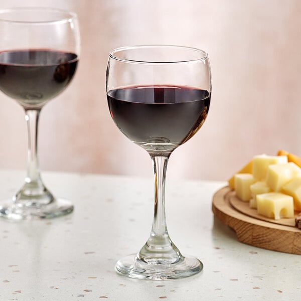 A close-up of a glass of red wine next to a plate of cheese on a table with another wine glass.