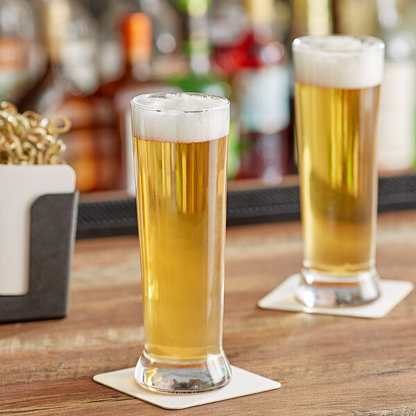 Two Acopa Pilsner glasses of beer on a wooden bar