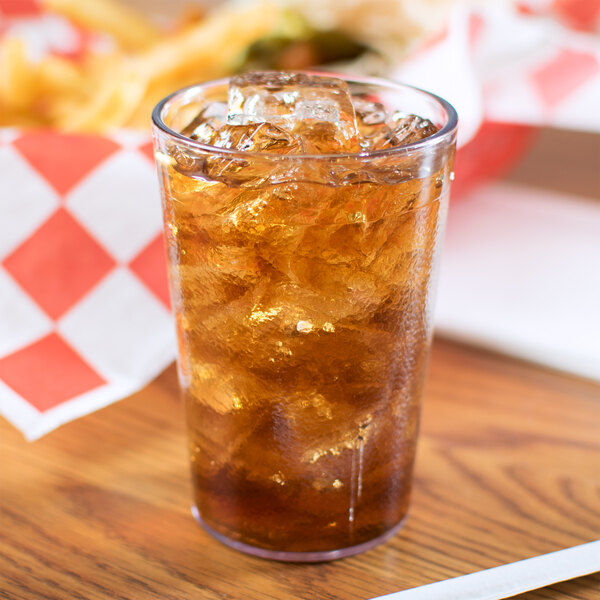A Carlisle clear plastic tumbler filled with ice tea on a table with ice cubes