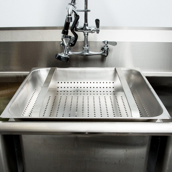 A stainless steel FMP pre-rinse basket with holes in a sink.