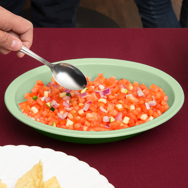 A hand holding a spoon over a bowl of chopped tomatoes.