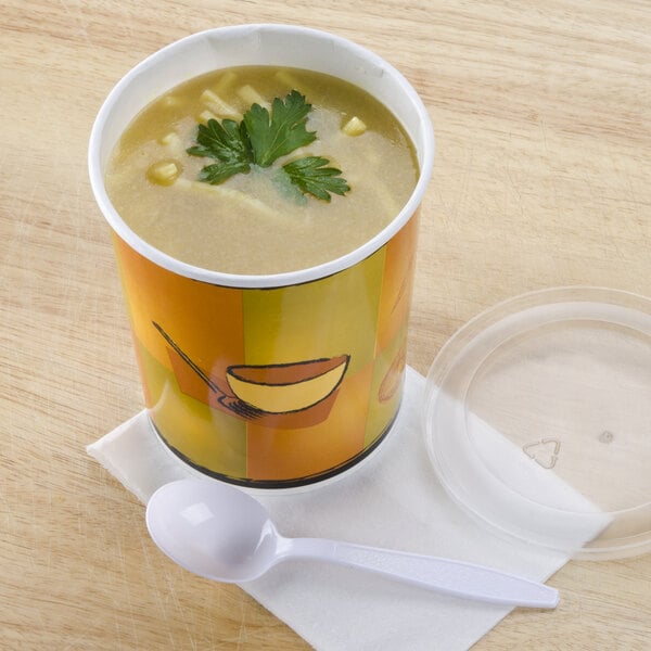 A Huhtamaki paper soup cup with a plastic lid on a white table with a spoon.