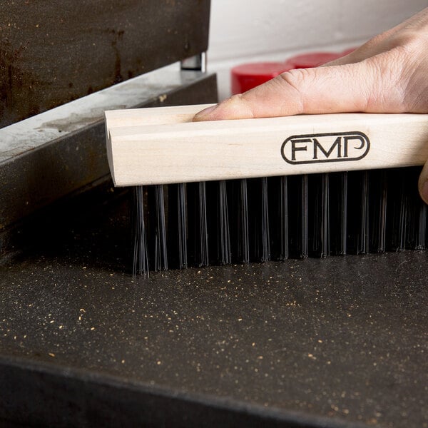 A hand holding an FMP grill cleaning brush head with medium bristles.
