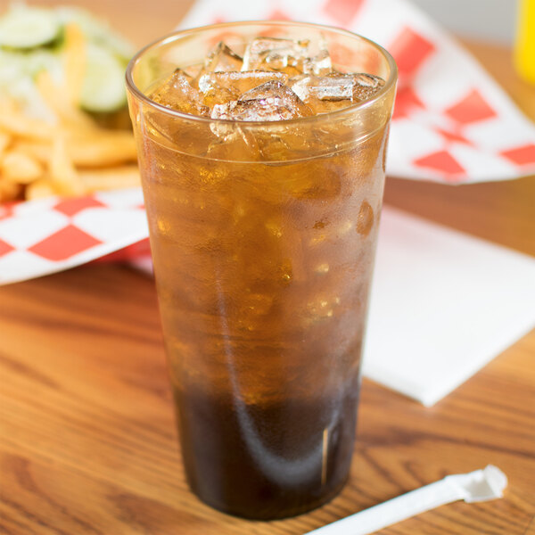 A Carlisle amber plastic tumbler filled with brown liquid and ice with a straw on a table with fries.