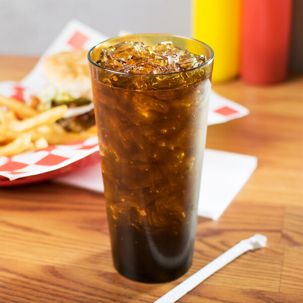 A Carlisle amber plastic tumbler with ice and soda on a table with a burger.