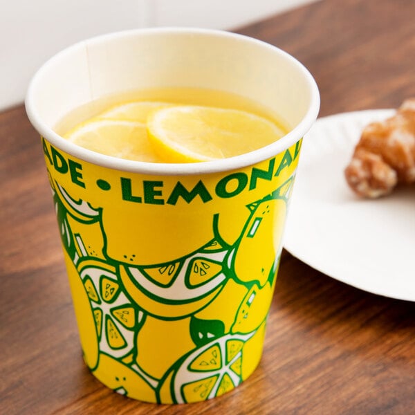 A 16 oz. squat paper lemonade cup on a counter with a cup of lemonade and a lemon slice on the rim.