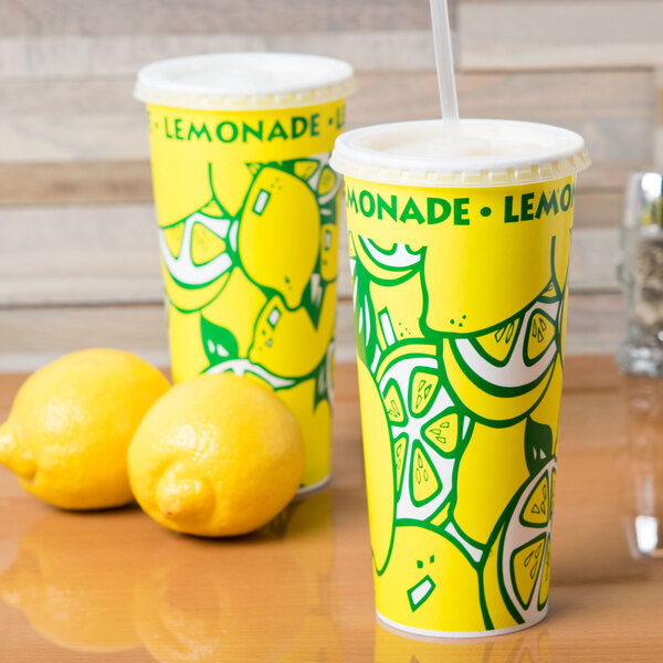 A yellow 24 oz. tall paper lemonade cup with a design next to two lemons.
