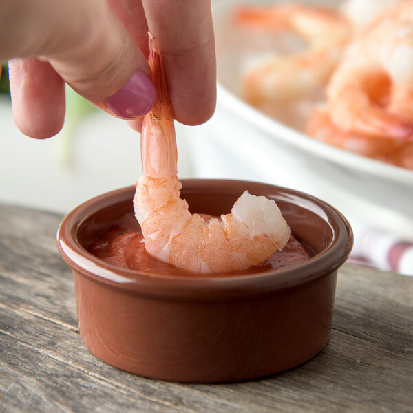 A person using a Carlisle Lennox brown plastic ramekin to dip a shrimp in sauce.