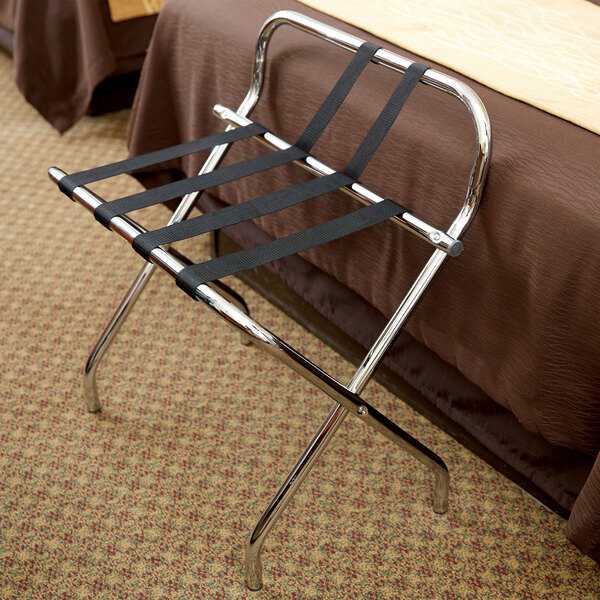 A black metal CSL luggage rack with black straps on it at the end of a bed.