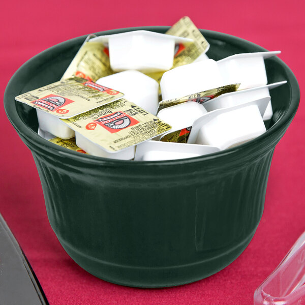A Tablecraft hunter green cast aluminum bowl filled with white and yellow packets on a hotel buffet counter.