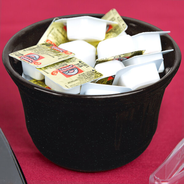 A Tablecraft black and green speckled metal bowl filled with sugar packets on a hotel buffet counter.