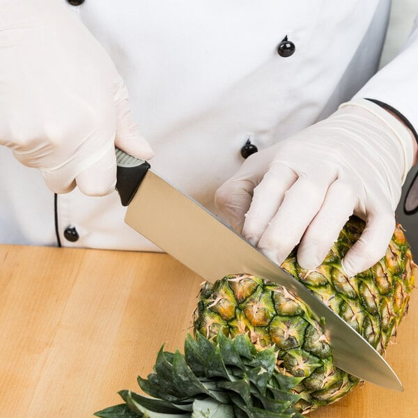 A person using a Dexter-Russell V-Lo chef knife to cut a pineapple.
