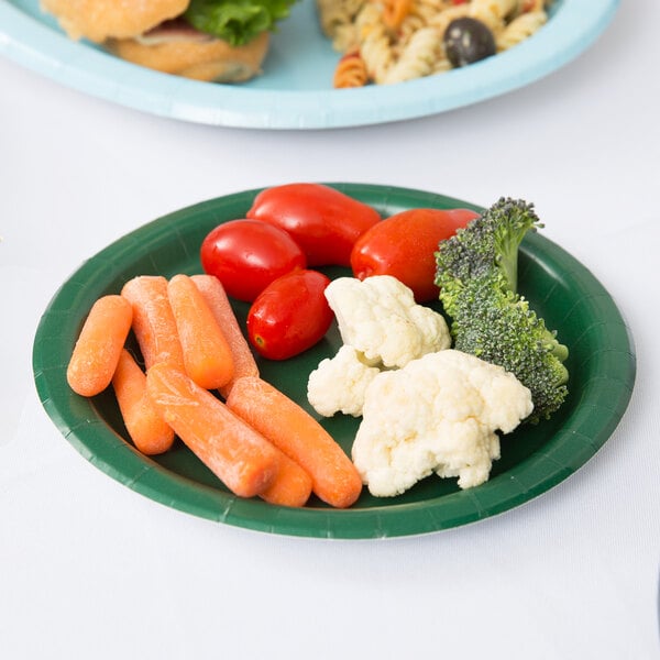 A plate of vegetables and pasta, including a carrot, on a green Hunter Green paper plate.