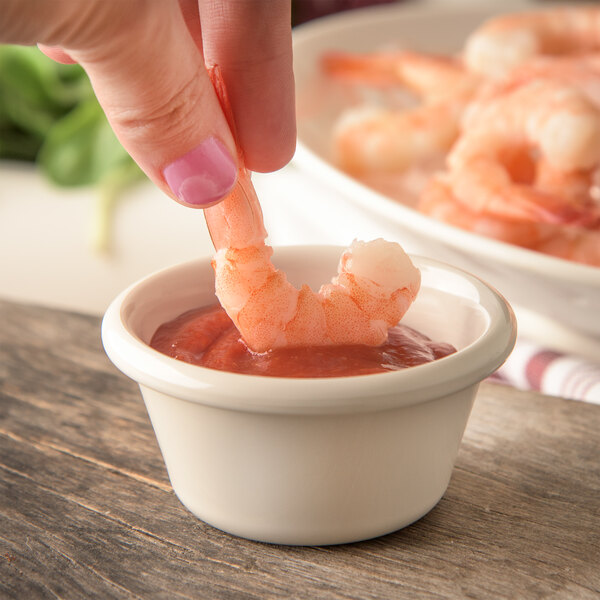 A person dipping a shrimp into a Carlisle bone white plastic sauce cup.