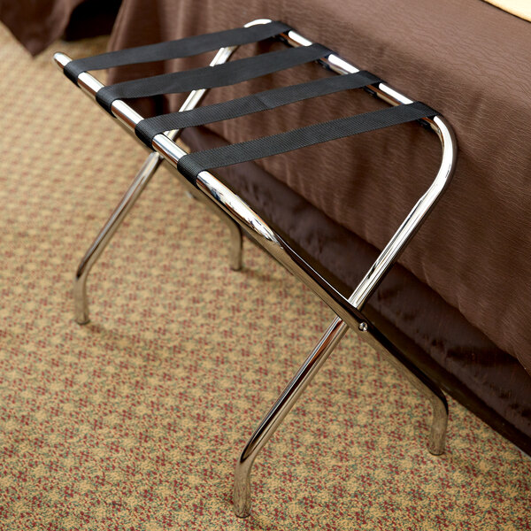 A CSL metal folding luggage rack with black straps on a bed.