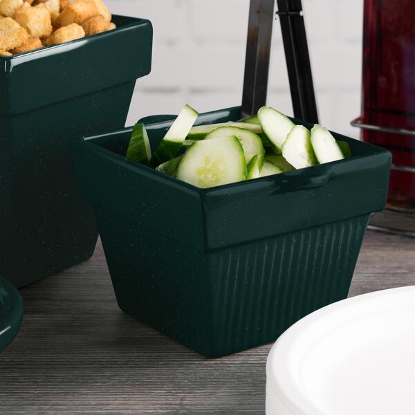 A green Tablecraft square condiment bowl with cucumbers inside.