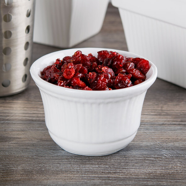 A Tablecraft white cast aluminum metal bowl filled with cranberries on a counter.