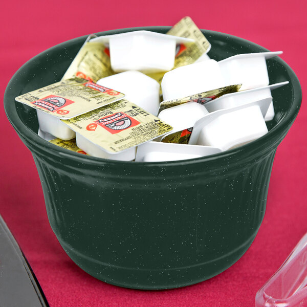 A hunter green cast aluminum bowl with white speckles on a counter filled with yogurt packets.