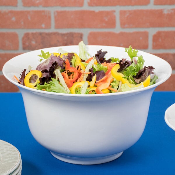 A Tablecraft white cast aluminum tulip salad bowl filled with salad including peppers and lettuce.