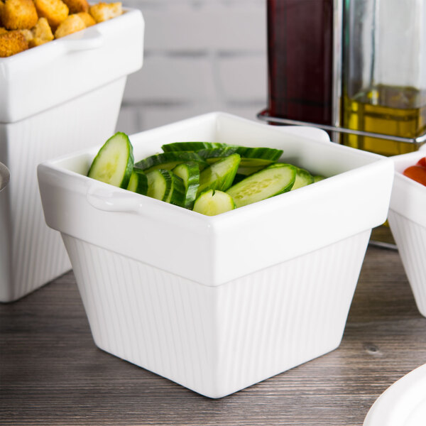 A white square Tablecraft condiment bowl with cucumber slices in it.