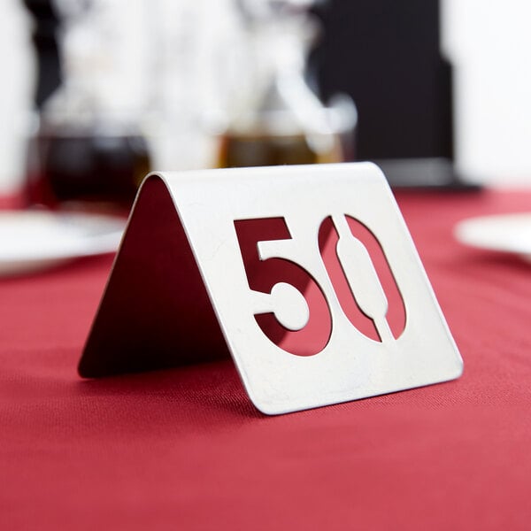 A stainless steel Tablecraft table number 50 on a table with a red tablecloth.