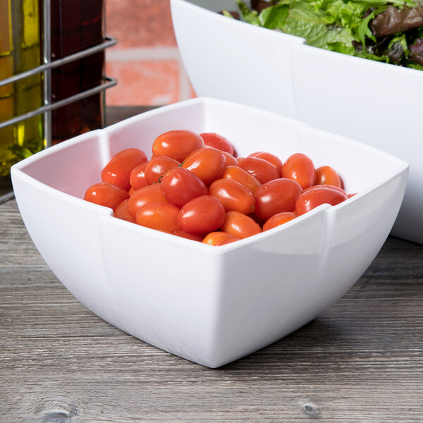 Two Carlisle white melamine serving bowls, one with cherry tomatoes and one with salad.