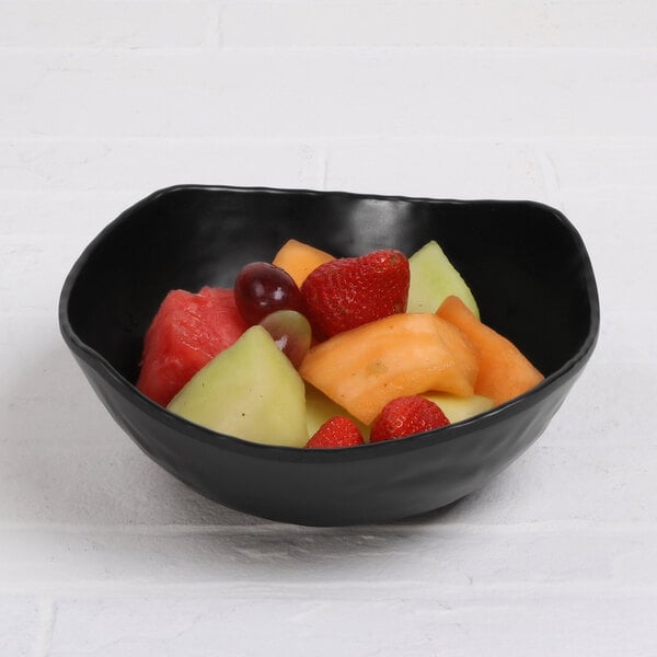 A black Elite Global Solutions squarish bowl filled with fruit on a white surface.