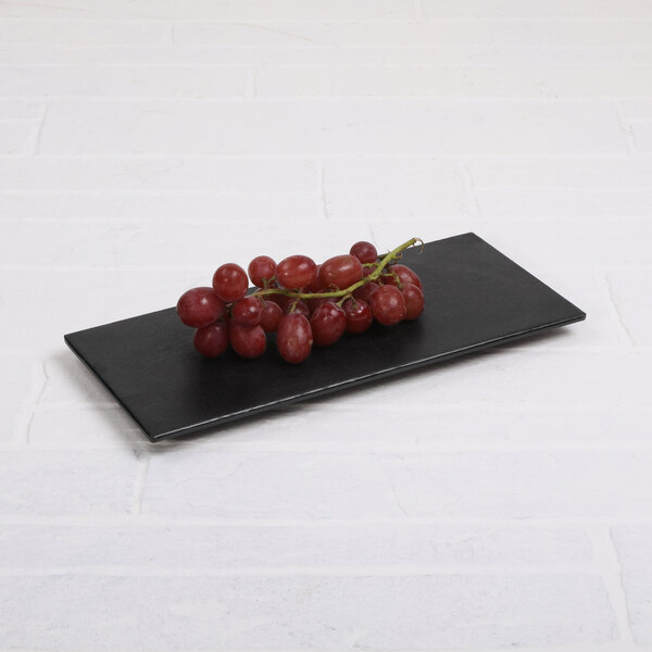 A black rectangular Elite Global Solutions melamine tray with a bunch of red grapes on it.
