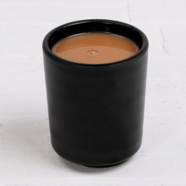 An Elite Global Solutions black melamine cup with brown liquid in it.