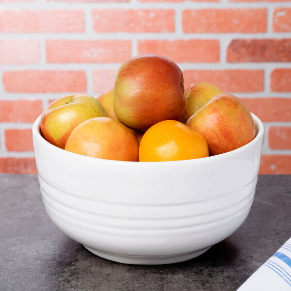 A white Tablecraft fruit bowl filled with apples and oranges.