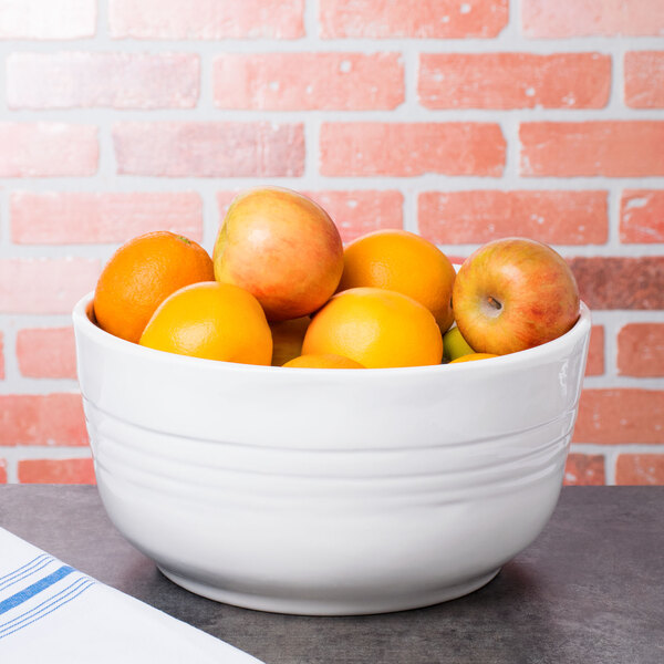 A white Tablecraft cast aluminum fruit bowl filled with oranges on a table.