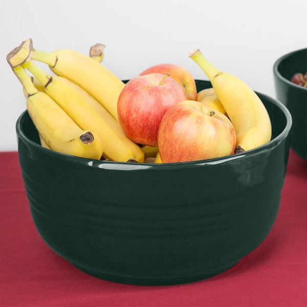 A Tablecraft hunter green cast aluminum fruit bowl filled with bananas and apples on a counter.